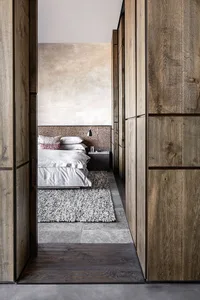 Modern minimalist bedroom with wood-paneled walls, concrete tiles, a bed with a soft bedspread and patterned pillows, and a b