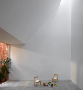 白色鋼材與混凝土地板，搭配兩張小型木椅及兒童玩具的簡約遊戲區。