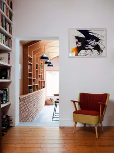 A cozy mid-century living room with a wooden floor, a colorful armchair, and a wall-mounted abstract painting.