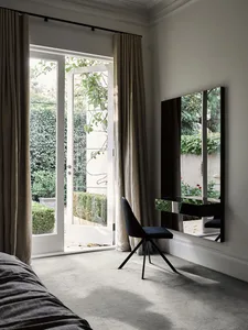 Minimalist bedroom featuring a metallic chair, glass mirror, and fabric curtains.
