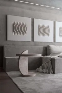 Modern minimalist living room featuring a grey upholstered sofa, a textured concrete side table, and three abstract white scu