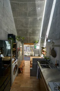 Modern minimalist kitchen with a concrete ceiling and floor, featuring a sink, stove, and washing machine