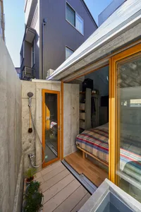 A minimalist residential space featuring concrete and wooden elements, with a bed and a shower.