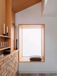 A minimalist window seat made of wood, featuring a cushion and framed by a wooden structure.