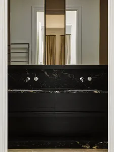 Modern bathroom with black marble counter and sink, silver faucet, and mirrored wall.