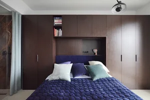 A modern bedroom featuring a bed with a blue comforter, white and green pillows, and a wooden storage unit with a shelf.