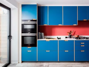 A modern kitchen with blue laminate cabinets, a red backsplash, and stainless steel appliances.