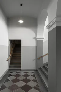 A modern interior hallway with concrete tiles, archways, and stairs.