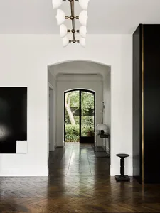 Modern entrance hallway with wooden chevron-patterned flooring, white walls, and a black and white abstract painting.