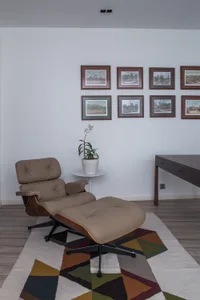 A modern interior lounge featuring a wooden armchair and ottoman with a potted plant.