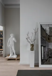 Modern living room with concrete floor and minimalist decor, featuring a large framed photograph and a vase with branches.