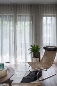 A modern living room with wooden furniture, white curtains, and a plant.