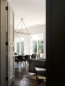 A modern living room with dark wood paneling, a grey sofa, and a dining area with a black chandelier.