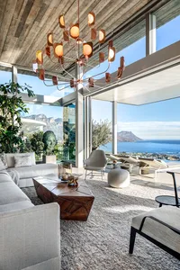 Modern luxury living room featuring a large sofa, coffee table, and a chandelier with a coastal view through large windows.