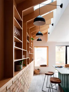 A cozy, modern residential kitchen with wooden shelves, black pendant lights, and a green kitchen island.