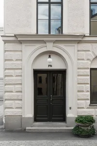 A white-clad residential entryway with stone steps and a green plant in a concrete pot.