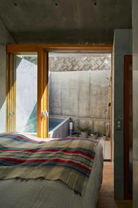 A minimalist bedroom with a concrete wall and wooden floor, featuring a bed with a striped blanket.