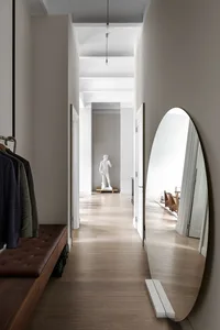 A modern corridor with floating lighting and an oval mirror against a minimalist backdrop.