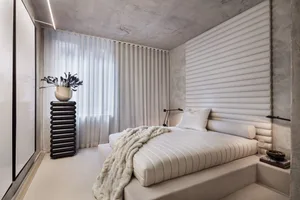 A minimalist bedroom featuring a concrete wall and a bed with white fabric bedding and a plush blanket.