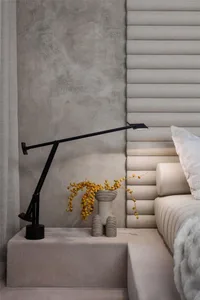 A modern minimalist bedroom with a textured cloth headboard and a sleek table lamp.