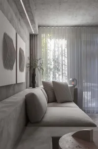 A modern minimalist interior with concrete walls, a gray sofa, and sheer curtains.