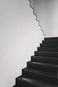 A modern black wooden staircase with embedded lighting against a white wall and minimalistic design.