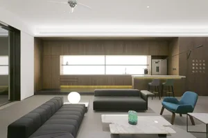 Modern living room with dark sofas, marble coffee tables, wood-paneled walls, and glass bar setup