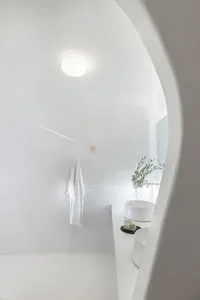 A minimalist bathroom with textured concrete walls and floor, a simple white sink, and a hanging robe.