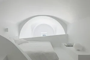 A minimalist bedroom with white walls, a white bed, and a white nightstand.