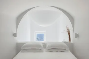 A minimalist bedroom with a white bed, minimalistic decor, and a view through an arched window