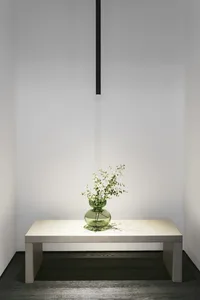 A minimalist interior design featuring a glass vase with greenery on a white table against a white backdrop.