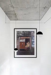 一張極簡攝影作品以相框展示在現代白色房間，搭配混凝土天花板。