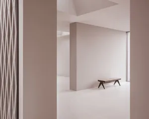 A minimalist white concrete space with a bench and a grid-like structure on the wall.