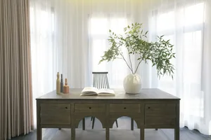 A modern home office setup featuring a wooden desk with a ceramic vase and green plant, and a wooden chair.