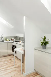 A modern kitchen with a wooden floor, white countertops, and stainless steel appliances.