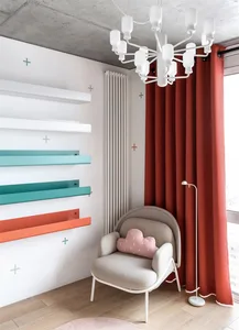 Modern living room with concrete walls, white and teal floating shelves, a beige armchair with a pink pillow, and a white flo