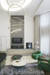 Modern living room featuring metal wire hanging lights, concrete fireplace, green accent chairs, and white coffee table with 
