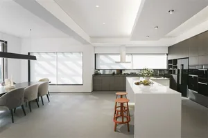 A modern residential kitchen with grey and black cabinets, an island with stools, and a dining area with grey chairs.
