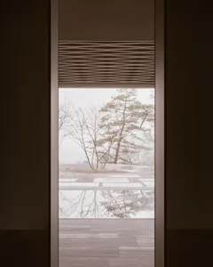 Metal blinds and a finished wooden floor frame a view of nature outside the window.