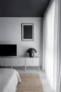 A minimalist bedroom featuring textured flooring, white furnishings, and a dark ceiling.