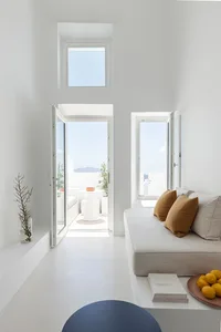 A cozy minimalist living room with white furniture and a window offering a serene view.