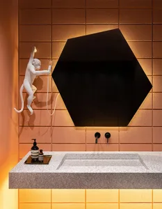 A modern bathroom with concrete finishes and hexagonal tiles, featuring a sink, mirror, and decorative monkey statue.