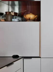 Modern kitchen with metallic finishes and white cabinets, featuring metallic pots and a wooden vase on the shelf.