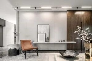 A modern living room with marble finishes, leather accent chair, and wooden cabinets.
