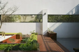 Modern minimalist terrace featuring wooden deck, concrete planters, and glass walls surrounded by greenery.