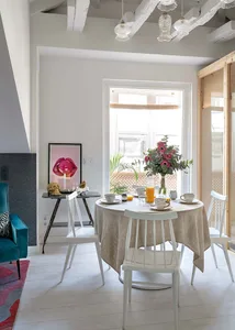 A contemporary breakfast nook with a round dining table, white chairs, and a cozy atmosphere, featuring a floral centerpiece