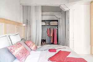 A minimalist bedroom featuring plastic curtains, clothes hangers, and neatly arranged bedding.