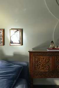 A modern bedroom featuring a blue couch, a wooden sideboard with intricate carvings, and framed artwork on the wall.