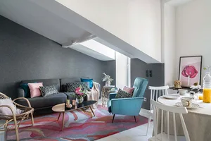 A modern living room with a mix of textures and colors, featuring a grey couch, blue armchair, and colorful rug.