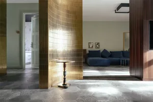 Modern living room with gold-tiled walls and a blue sofa.